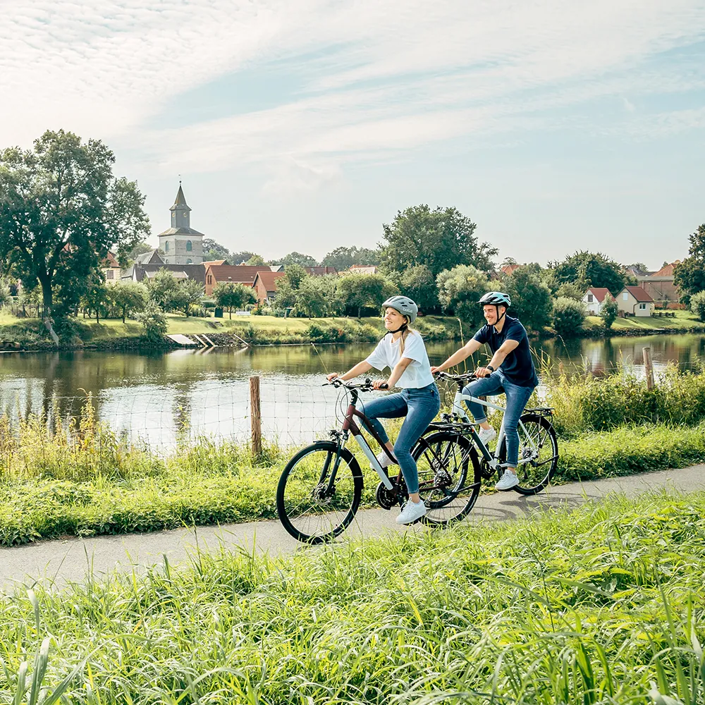 Zwei Radfahrer auf einem Uferweg mit Kirche im Hintergrund